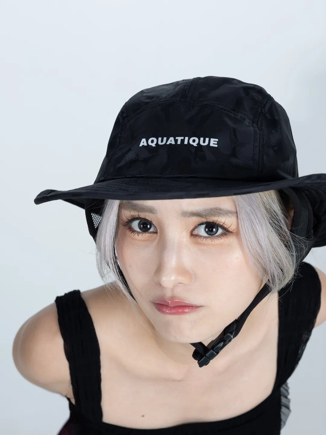 Close-up of a woman in a black camouflage AQUATIQUE bucket hat with the AQUATIQUE logo and chin cord
