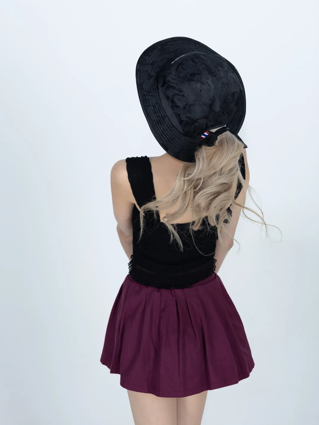 A woman seen from behind in a black camouflage AQUATIQUE bucket hat, long blonde hair falling out at the back below a Thai flag tab