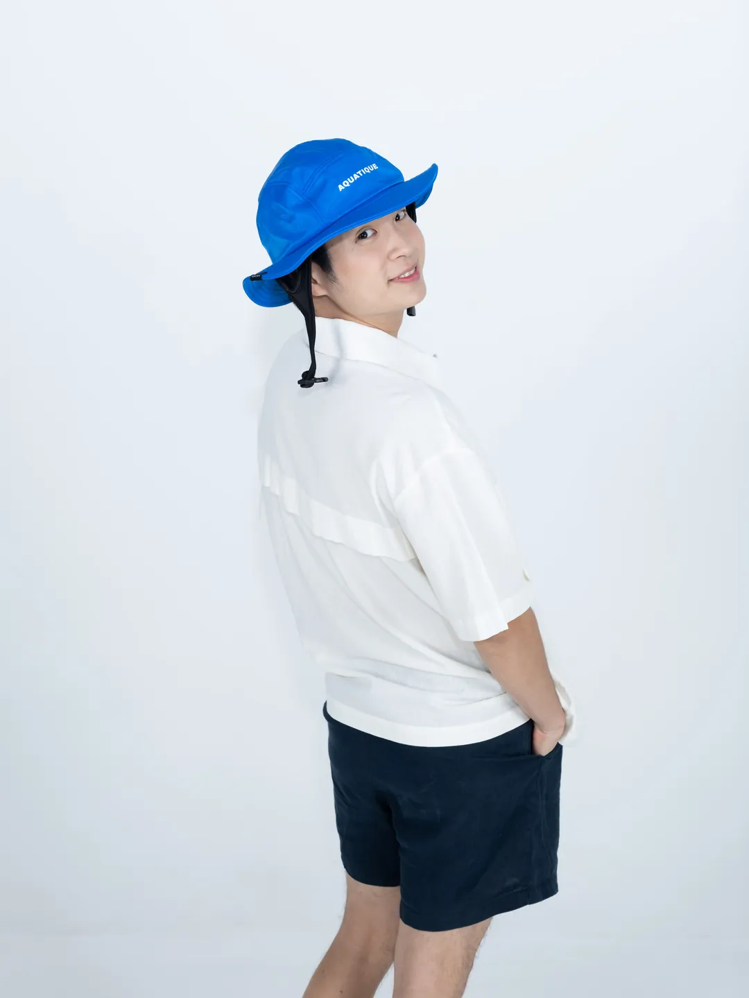 A man in a bright blue AQUATIQUE bucket hat looking back over his shoulder