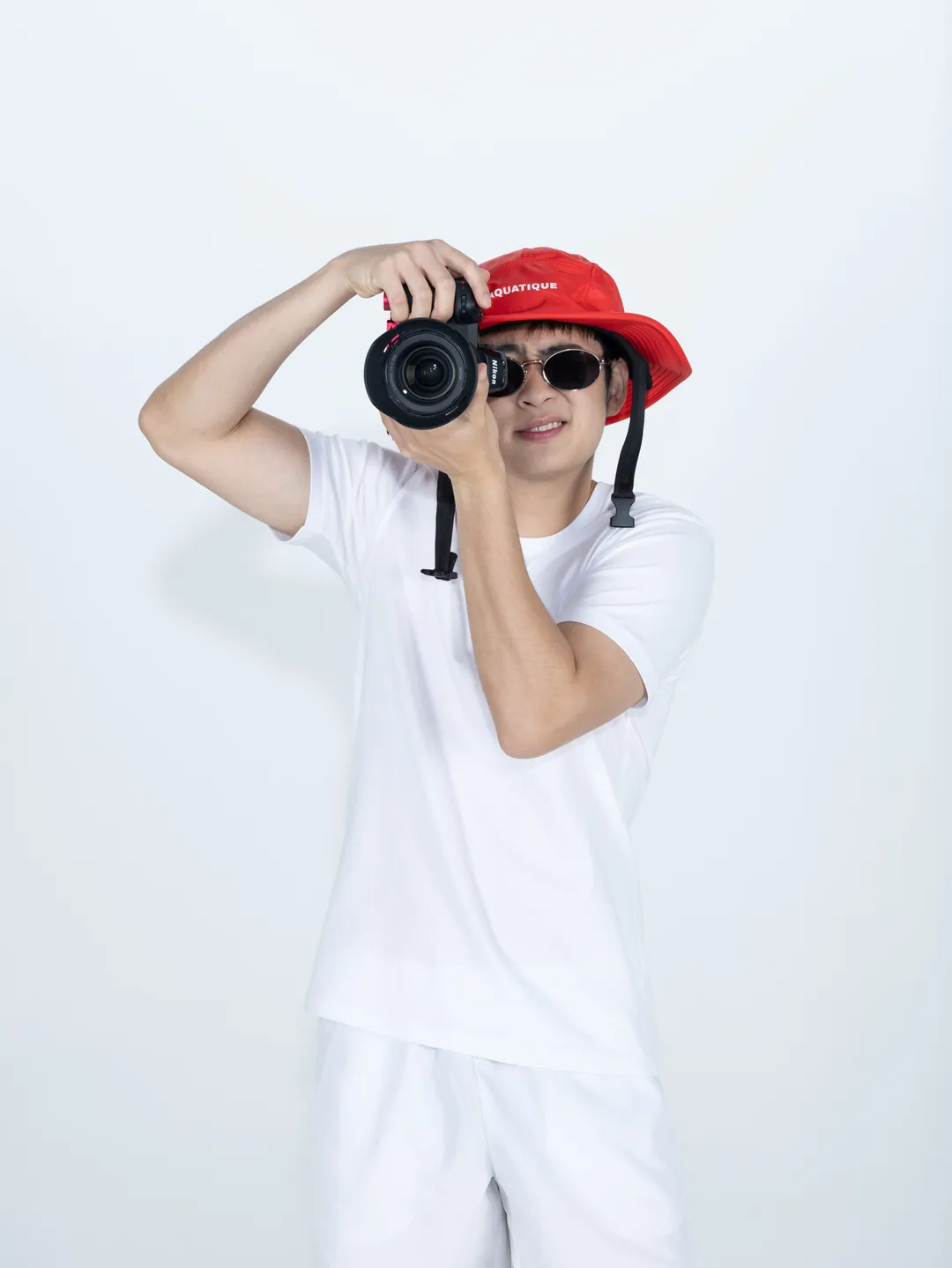 A man in a red AQUATIQUE bucket hat and white clothes, taking a photo with a camera